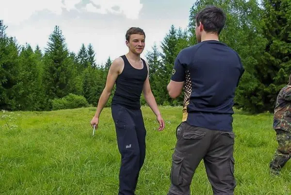 Zwei Personen stehen auf einer Wiese, eine hält ein Messer in der Hand