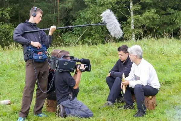 Drei Personen sitzen auf Baumstümpfen, während ein Kamerateam filmt