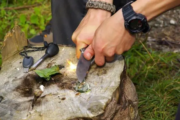 Feuerstahl erzeugt Funken auf Zunder während ein Messer verwendet wird