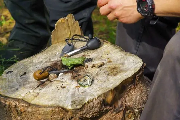 Feuerstahl und Zunder liegen auf einem Baumstumpf, Hände bereiten sich vor