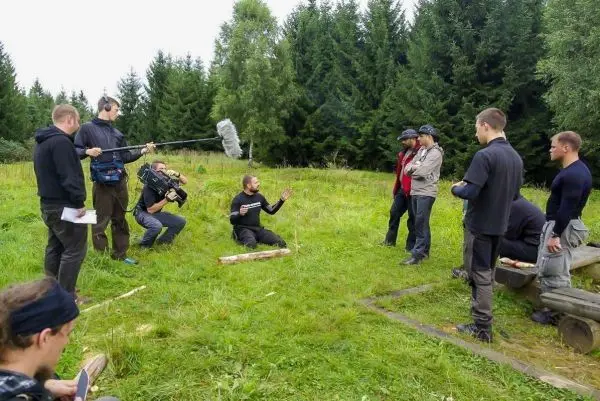Gruppe diskutiert im Freien, während Kamerateam Aufnahmen macht