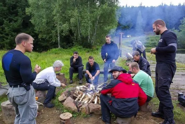 Gruppe sitzt um ein Feuer und bereitet Essen zu beim Survival Training