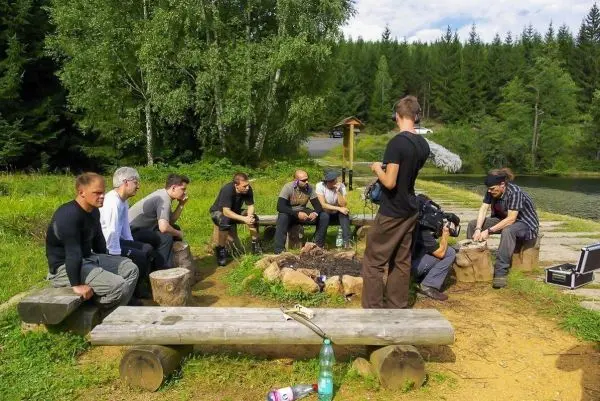 Gruppe sitzt um ein kleines Bodenfeuer auf Baumstämmen und diskutiert