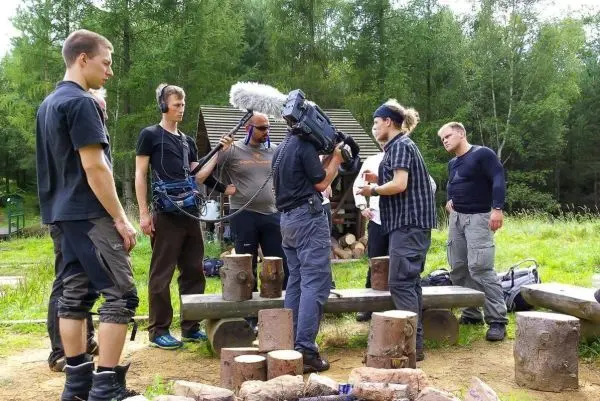 Gruppe von Personen steht um einen Tisch aus Baumstämmen beim Filmen