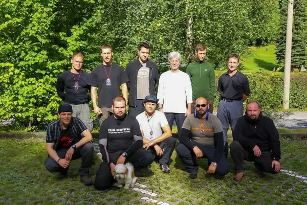 Gruppierung von zehn Personen und einem Hund auf einer Wiese, umgeben von Bäumen