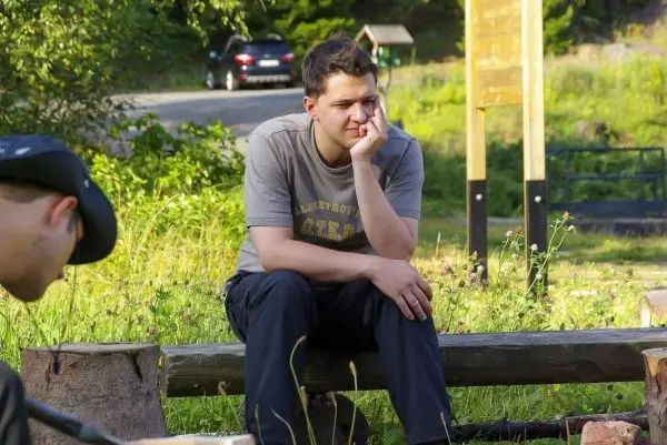 Junger Mann sitzt nachdenklich auf einer Holzbank in der Natur
