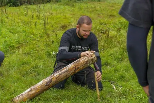 Mann bearbeitet Holzstück mit einem Messer auf dem Boden