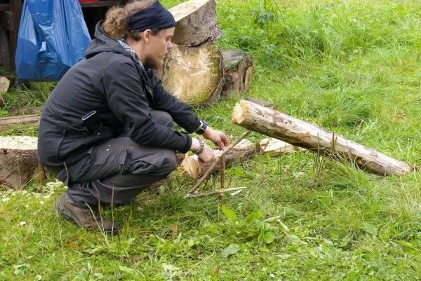 Mann bearbeitet Holzstück mit einem Messer auf dem Boden