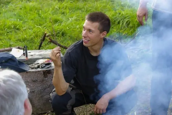 Mann hält einen Stock in der Hand, Rauch steigt aus einem kleinen Feuer auf