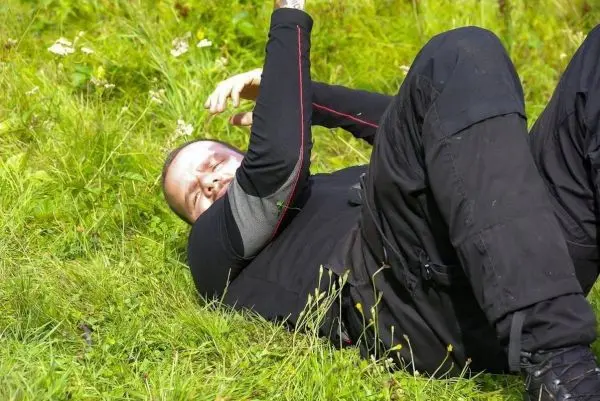 Mann liegt auf dem Gras und hält sich den Kopf mit einer Hand