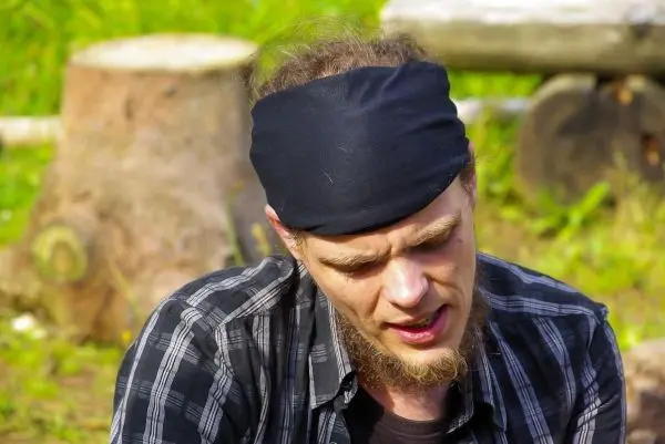 Mann mit schwarzem Stirnband sitzt vor Baumstümpfen und konzentriert sich