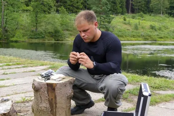 Mann sitzt auf einem Baumstumpf und bereitet Angelausrüstung vor