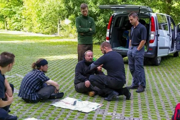 Mann zeigt Erste-Hilfe-Techniken an sitzendem Teilnehmer auf einer Decke
