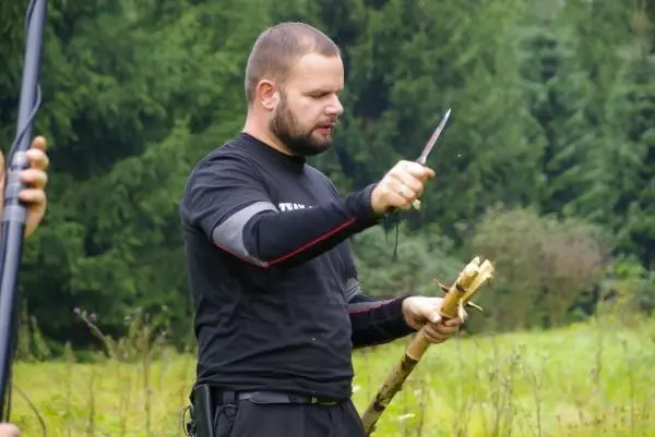 Messer schneidet einen Stock in einer Wiese mit Bäumen im Hintergrund