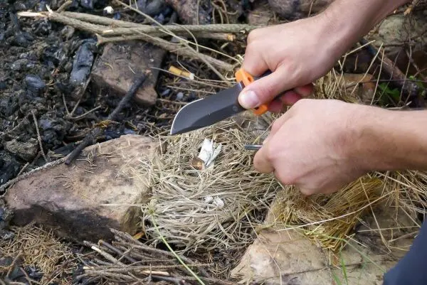 Messer schneidet Zunder in einem Zundernest aus trockenem Gras