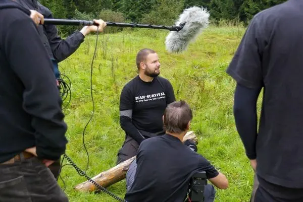Mikrofon wird über sitzendem Mann in der Natur gehalten, Kamera auf ihn gerichtet