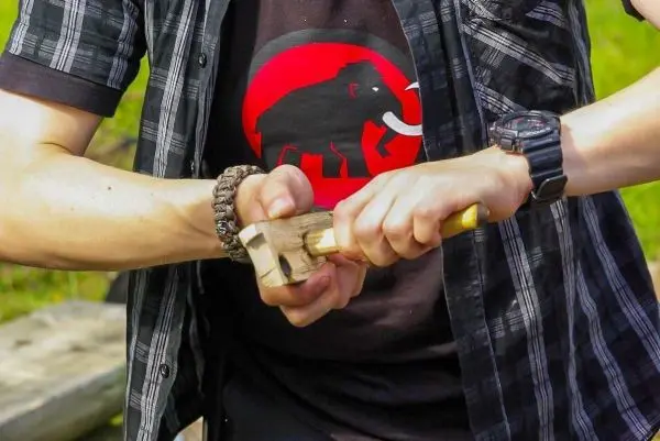 Person bearbeitet Holzstück mit einem Werkzeug beim Überlebenstraining