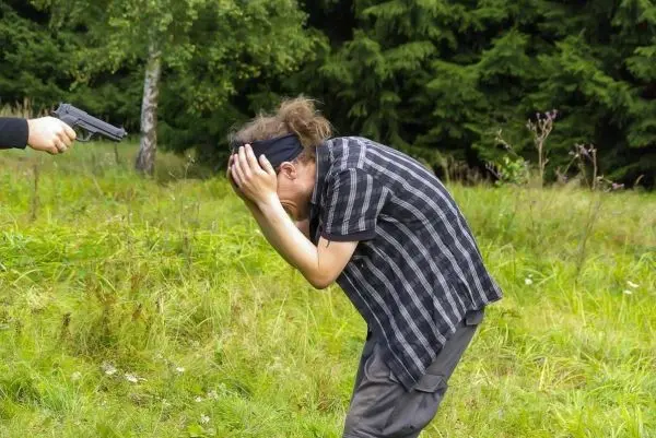 Person hält sich den Kopf und duckt sich im Gras