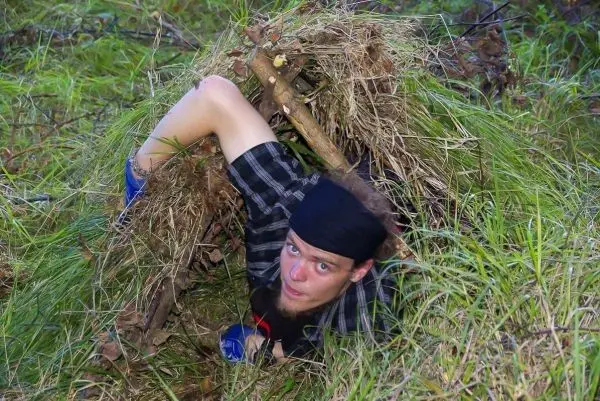 Person kriecht aus einer selbstgebauten Unterkunft im Gras