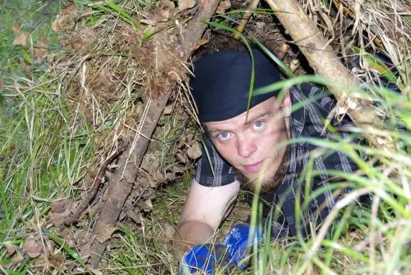 Person kriecht aus einer selbstgebauten Unterkunft im Gras