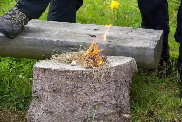 Person steht neben brennendem Nest auf Baumstumpf beim Überlebenstraining