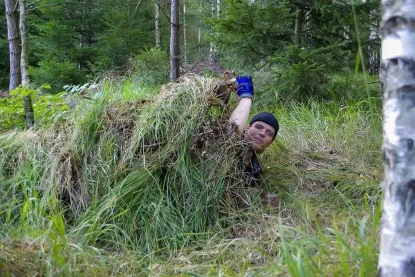 Person versteckt sich unter Gras und Ästen im Wald