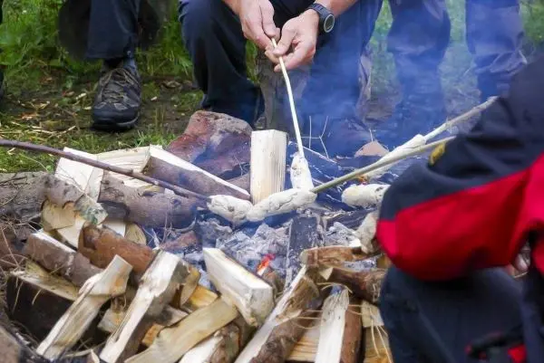 Zunder glimmt in einem kleinen Bodenfeuer, während Stöcke über der Glut gehalten werden