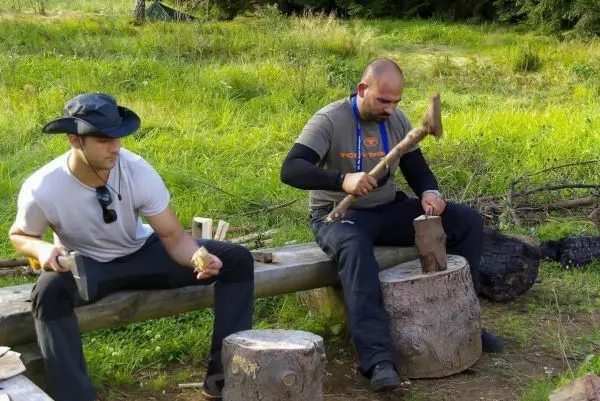 Zwei Personen bearbeiten Holz mit einem Messer und einer Axt auf Baumstümpfen