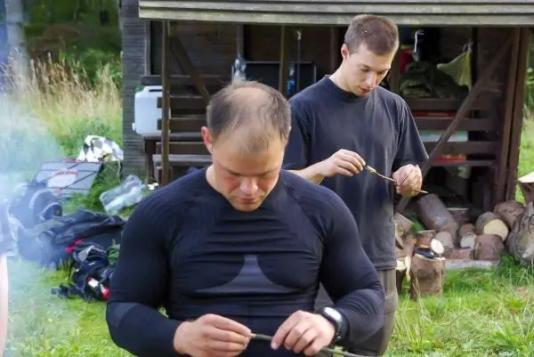 Zwei Personen bearbeiten Holzstücke mit kleinen Werkzeugen im Freien