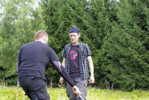 Zwei Personen stehen in einer Wiese, eine hält einen Stock in der Hand