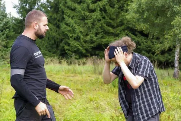 Zwei Personen stehen in einer Wiese, eine Person hält sich ein Tuch vor die Augen