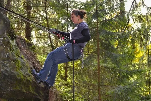 Abseilen an einem Felsen mit Sicherungsseil und Klettergurt in einem Wald