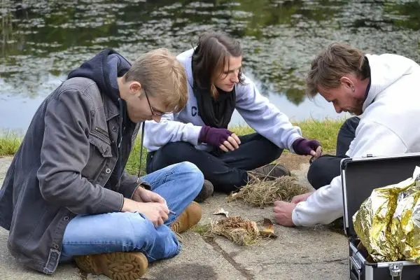Drei Personen bereiten Zunder auf dem Boden vor, während ein Koffer daneben steht