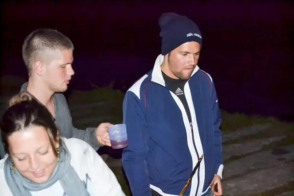 Drei Personen stehen in der Dunkelheit, einer hält ein Getränk in der Hand