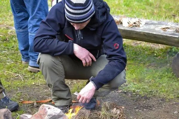 Feuerstahl entzündet Zunder neben kleinen Flammen auf dem Boden