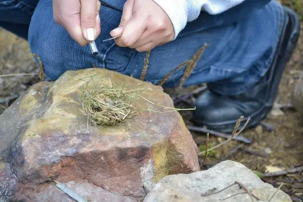 Feuerstahl erzeugt Funken auf Zundernest aus Gras auf einem Stein