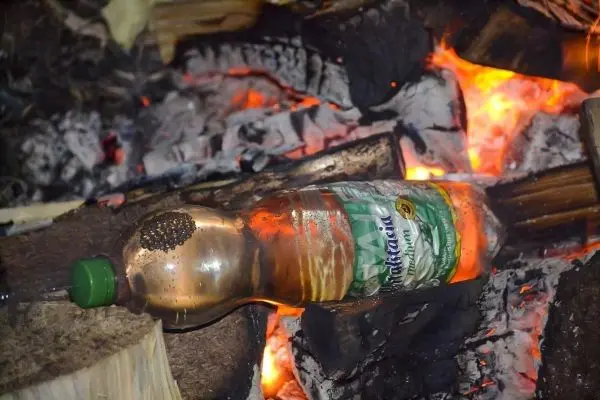 Flasche liegt auf glühenden Holzscheiten in einem kleinen Feuer