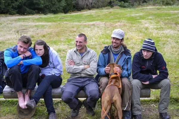 Fünf Personen sitzen auf einer Holzbank, ein Hund liegt neben einem Mann