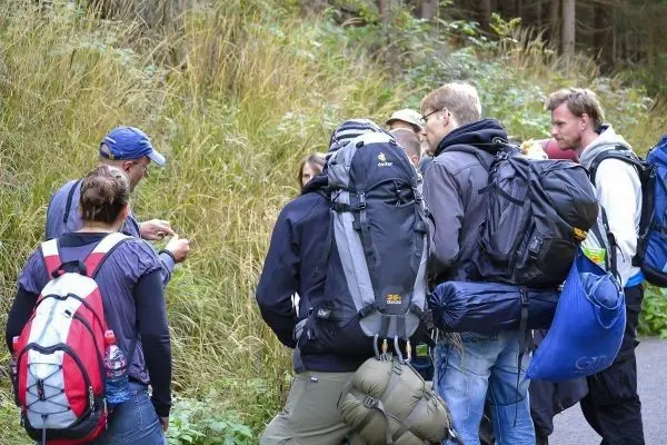 Gruppe mit Rucksäcken steht an einem Weg und betrachtet eine Karte