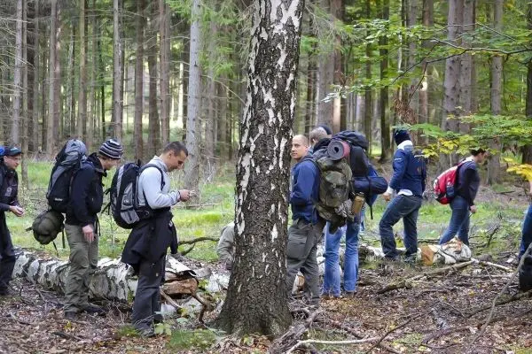 Gruppe mit Rucksäcken steht im Wald und betrachtet den Boden
