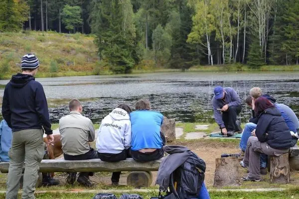 Gruppe sitzt auf einer Bank am Ufer eines Sees und beobachtet eine Demonstration