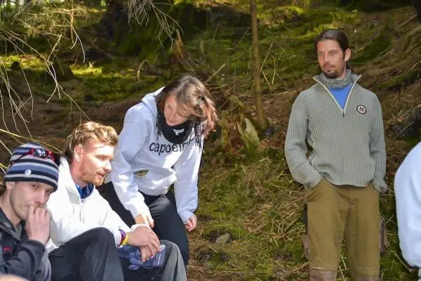 Gruppe sitzt im Wald auf dem Boden, eine Person beugt sich zu einer anderen