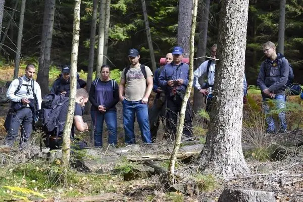 Gruppe von Personen beobachtet einen Trainer im Wald beim Überlebenstraining