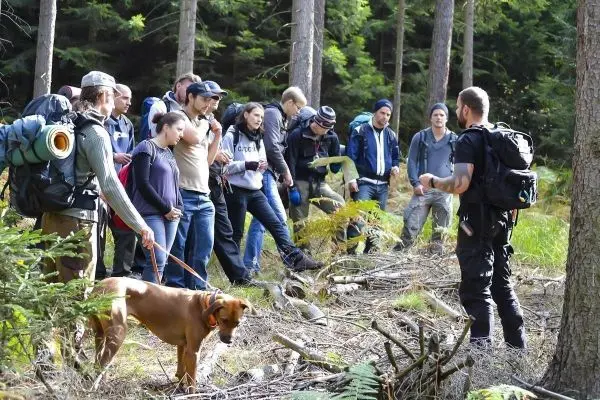 Gruppe von Personen mit Rucksäcken hört einem Referenten im Wald zu