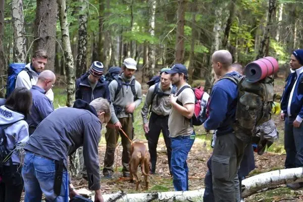 Gruppe von Personen mit Rucksäcken um einen Hund im Wald versammelt