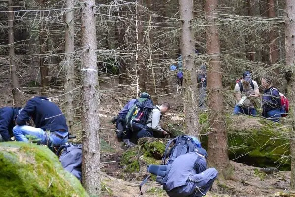 Gruppenmitglieder untersuchen den Boden im Wald, Rucksäcke liegen verstreut