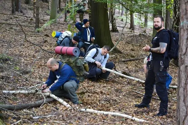 Gruppierung arbeitet im Wald an Holzstücken, einige nutzen Messer zur Bearbeitung