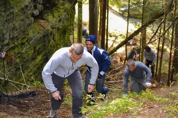 Gruppierung von Personen beim Aufstieg durch bewaldetes Gelände mit Felsen