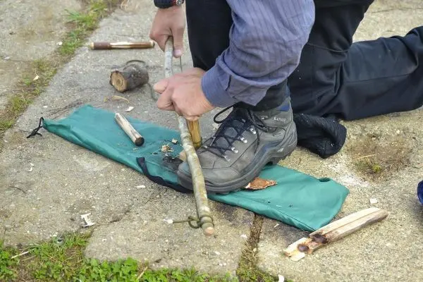 Holzstück wird mit einem anderen Stock bearbeitet, um Zunder zu erzeugen