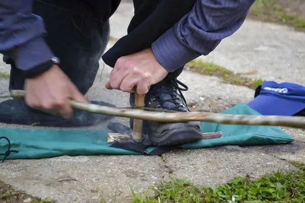 Holzstück wird mit einem Stock durch Reibung bearbeitet, um Glut zu erzeugen